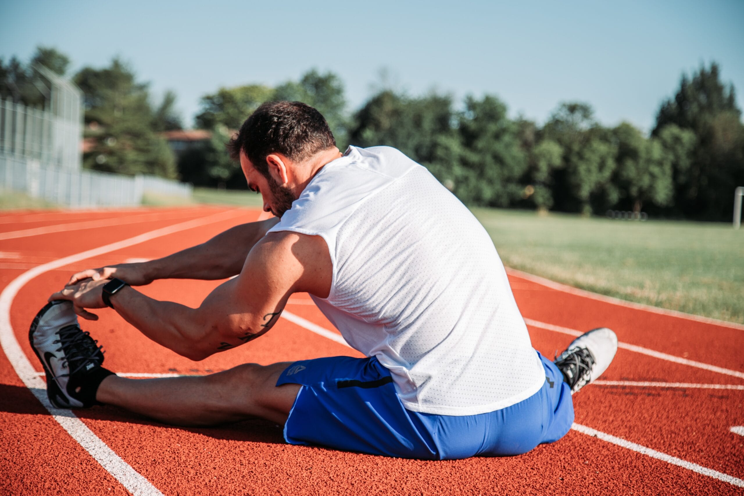 A man stretching his legs on a track and field oval.