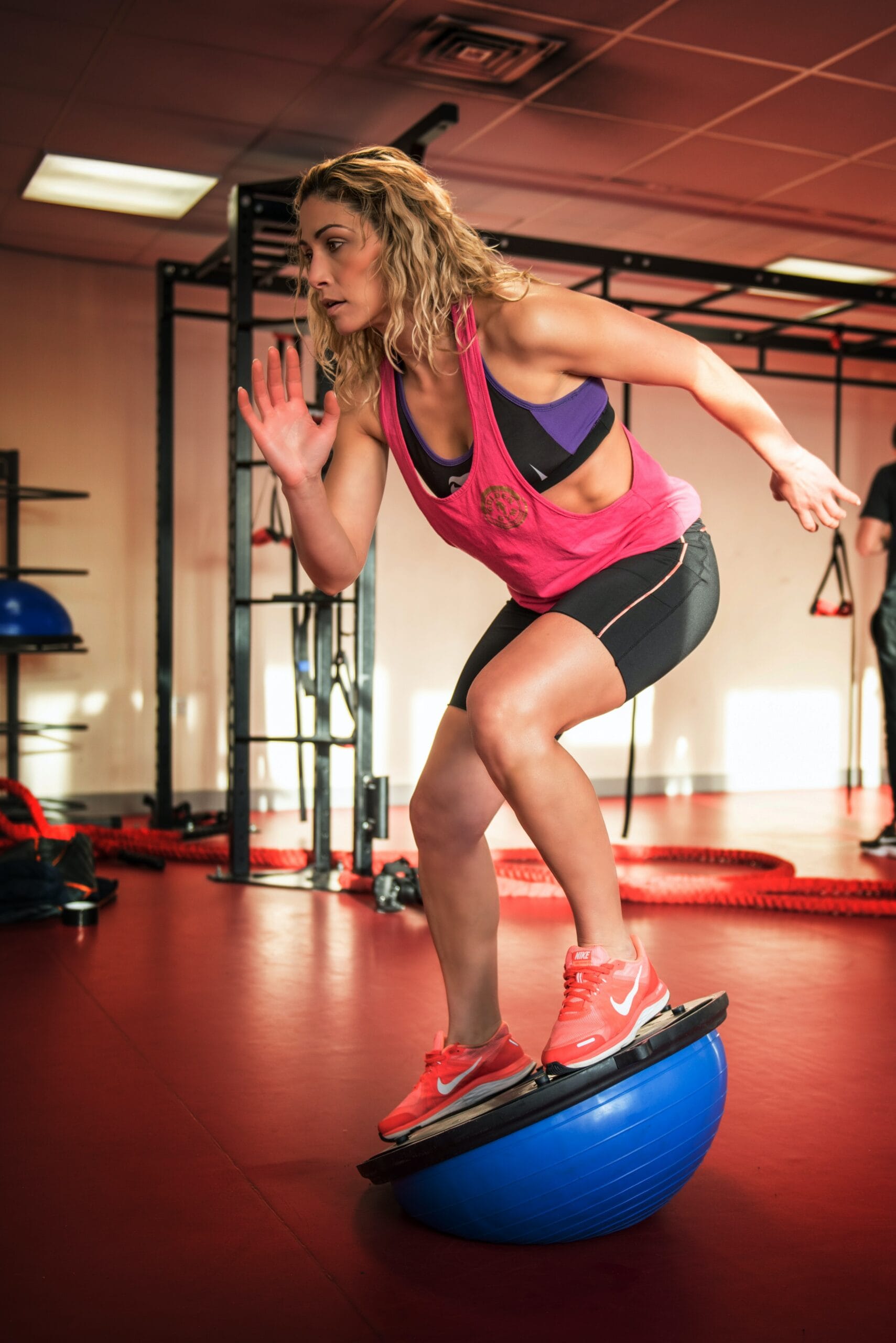 A woman balances on a Bosu ball as part of her athletic conditioning routine under the supervision of a sports physiotherapist.